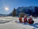 Aktiver Familienurlaub am Achensee Kinder spielen im Schnee vor schneebedeckten Bergen bei sonnigem Wetter