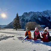 Kinder spielen im Schnee vor schneebedeckten Bergen bei sonnigem Wetter