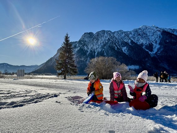 Kinder spielen im Schnee vor schneebedeckten Bergen bei sonnigem Wetter