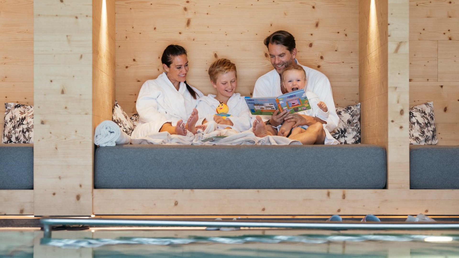 Family in bathrobes relaxing on lounge near indoor pool