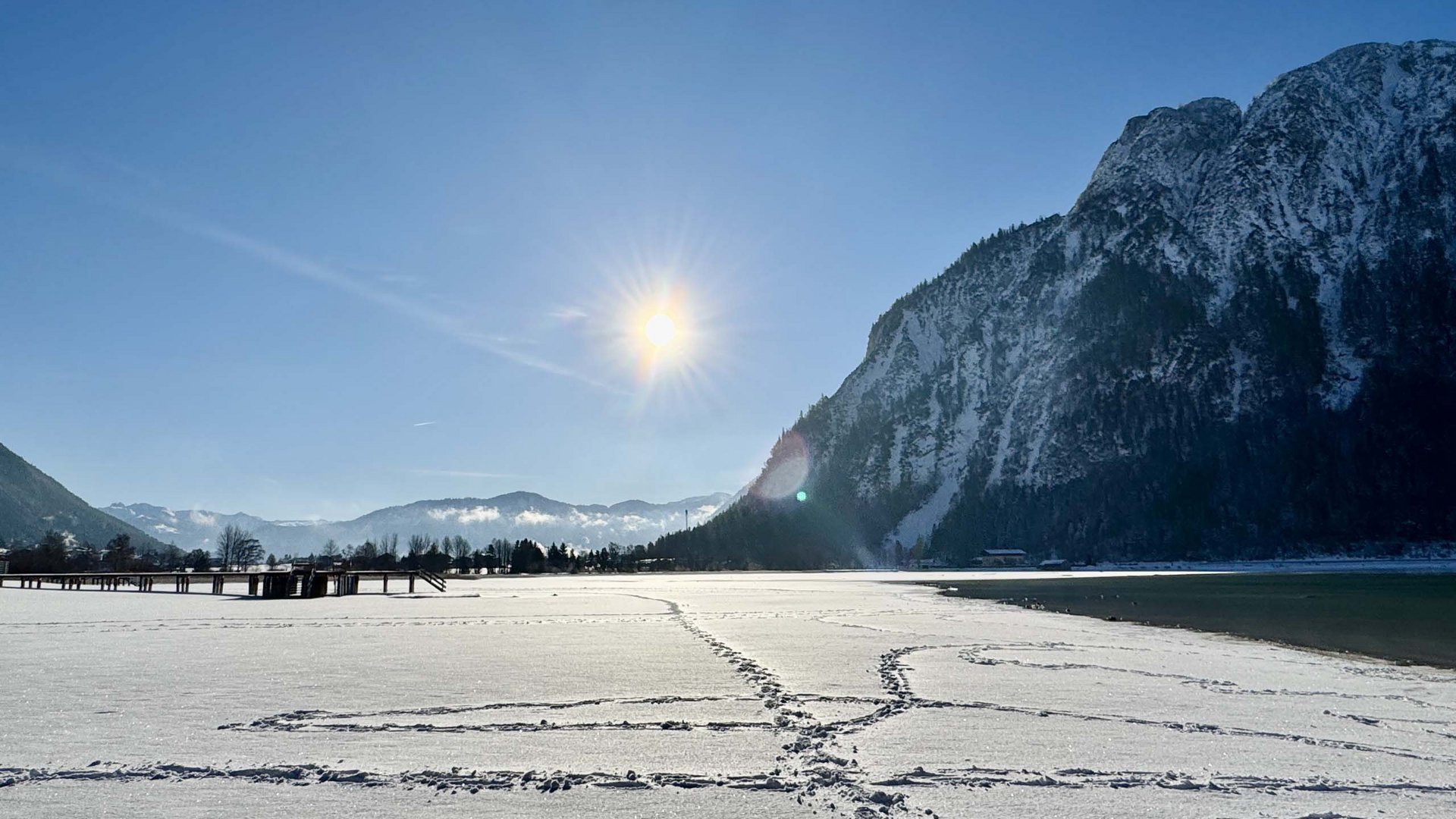 Snow-covered lake with footprints and mountain under clear sunny sky