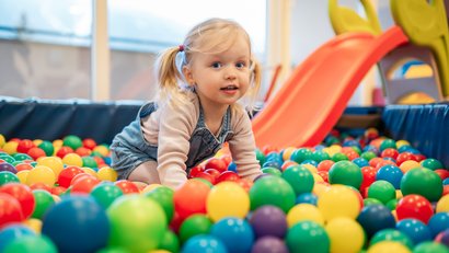 Little girl playing in a ball pit with a colorful slide in the background