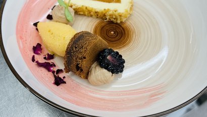 Artfully plated dessert with blackberries, various creams, and cake pieces