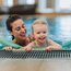 Mother and daughter smiling in pool with swimming noodles