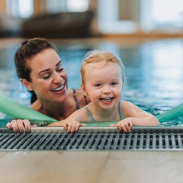 Mother and daughter smiling in pool with swimming noodles
