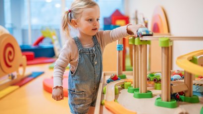 Mädchen spielt mit einem hölzernen Spielzeugauto in einem bunten Spielzimmer