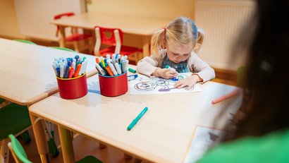 Child coloring with markers at a table in a classroom