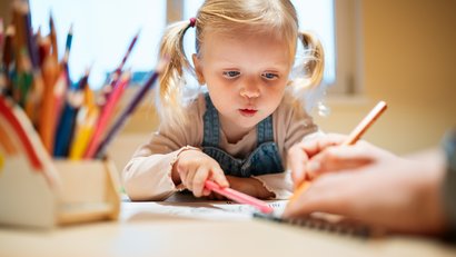 Kleines Mädchen malt konzentriert mit bunten Stiften am Tisch