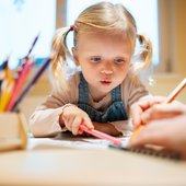 Kleines Mädchen malt konzentriert mit bunten Stiften am Tisch