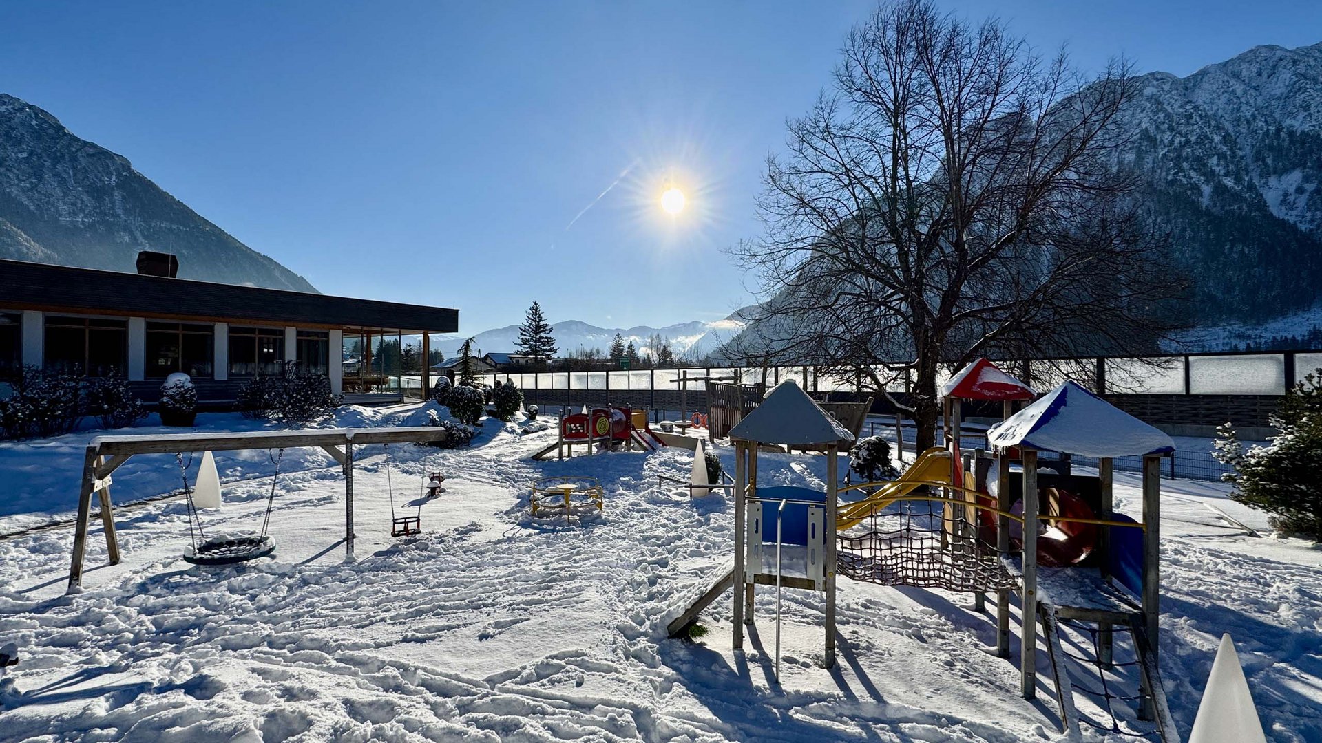 Snow-covered playground with slide and swing under sunny mountain sky