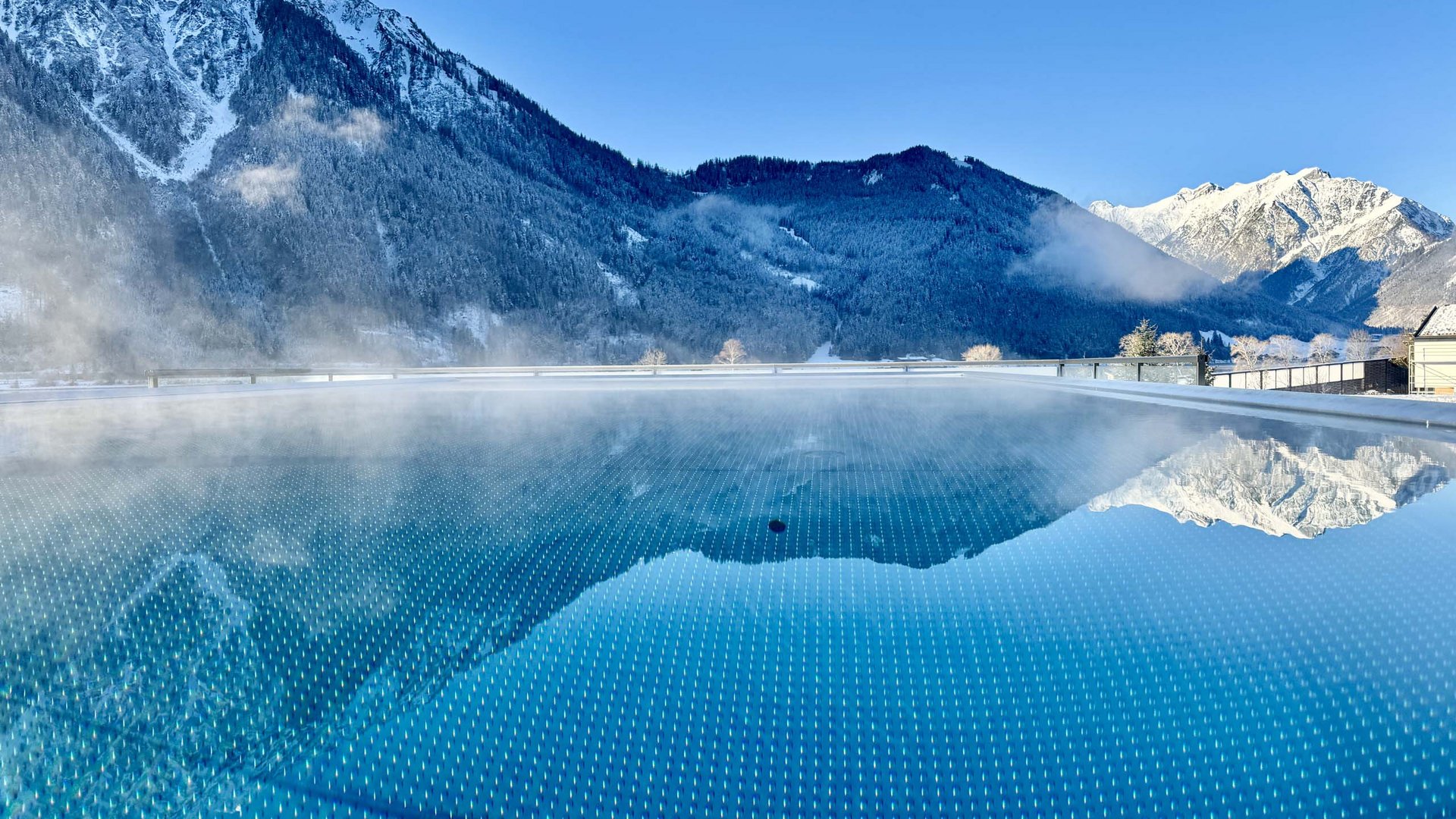 Hot pool with steam facing snow-covered mountains under clear sky
