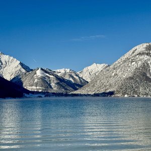 Snow-covered mountains reflected in a calm lake under clear blue sky