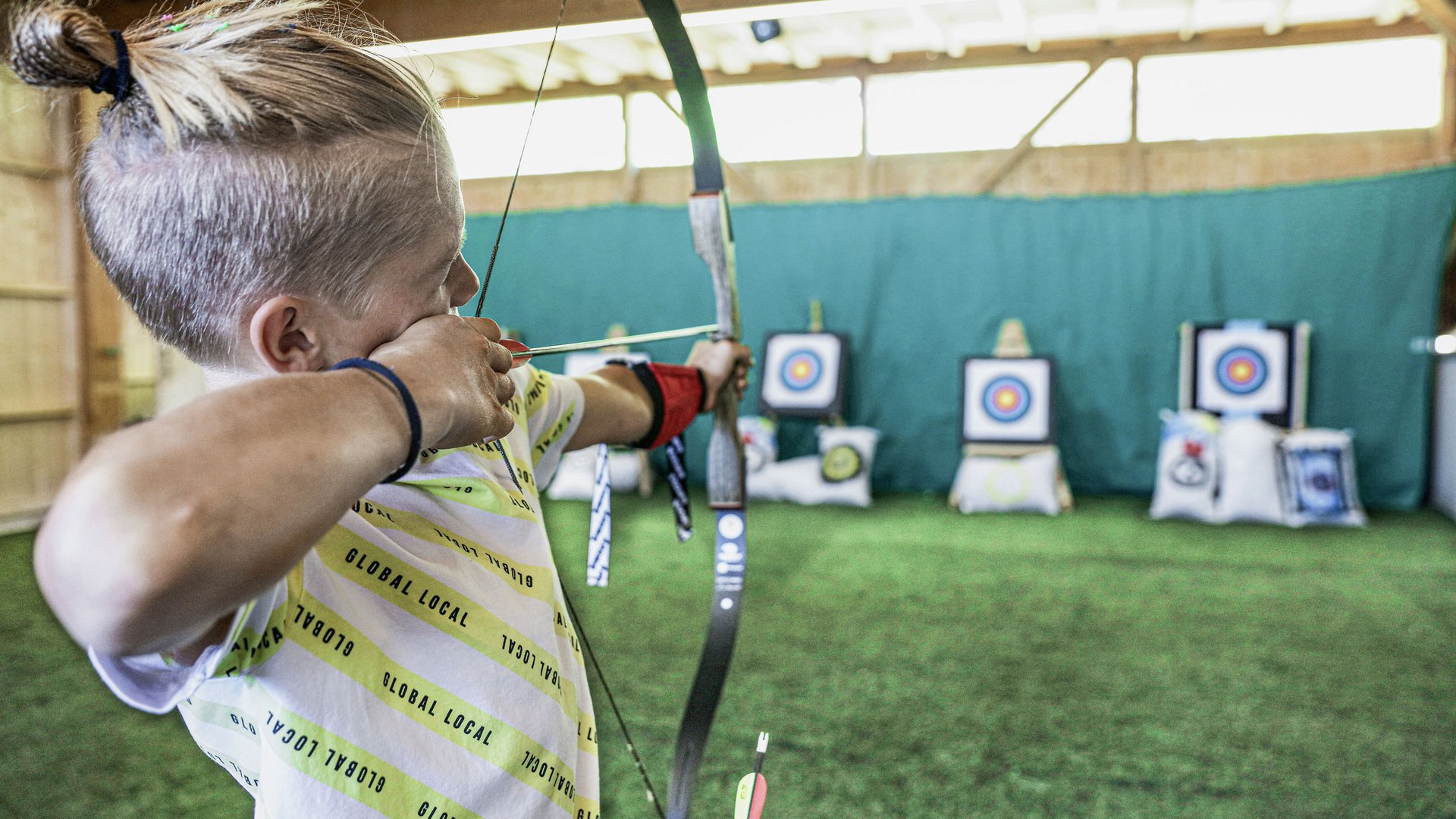 Child shooting a bow at targets indoors