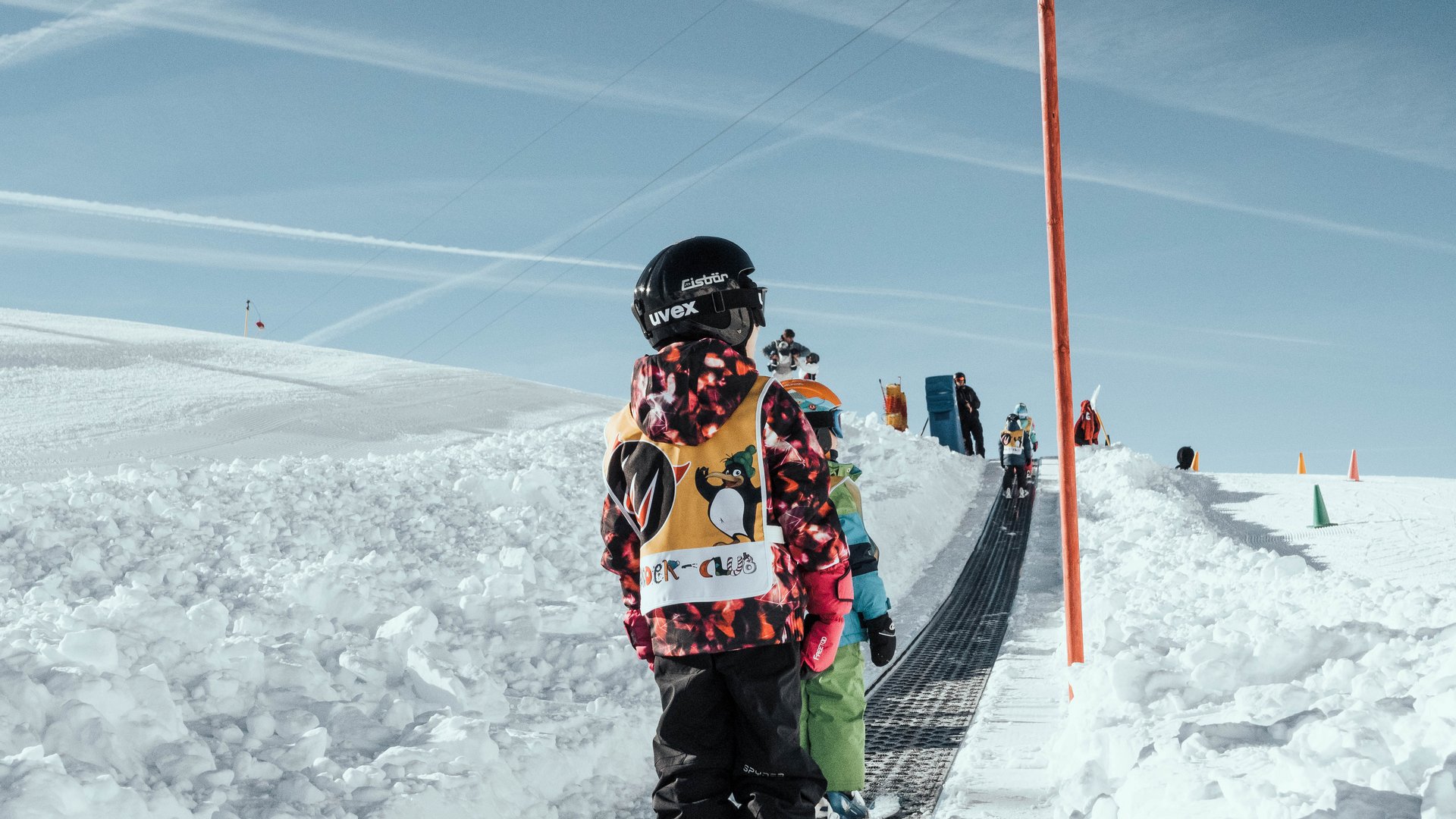 Children in ski gear standing on a magic carpet lift in the snow