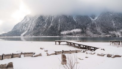 Snow-covered lake with wooden pier and foggy forested mountain