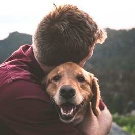 Man hugging a smiling Golden Retriever outdoors