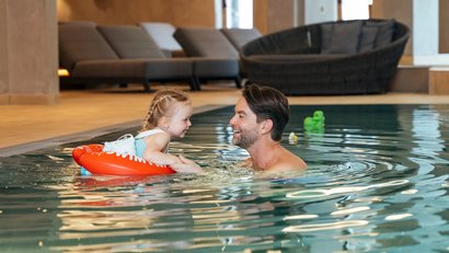 Father and daughter smiling together in indoor pool with red swimming ring