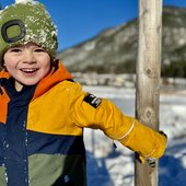Lachendes Kind in bunter Winterjacke und grüner Mütze im Schnee
