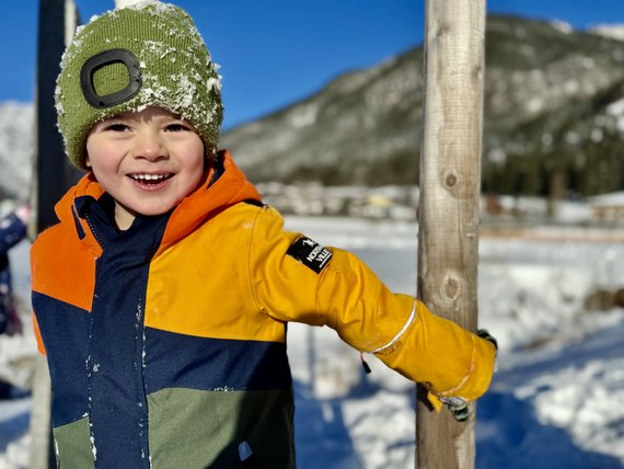 Lachendes Kind in bunter Winterjacke und grüner Mütze im Schnee